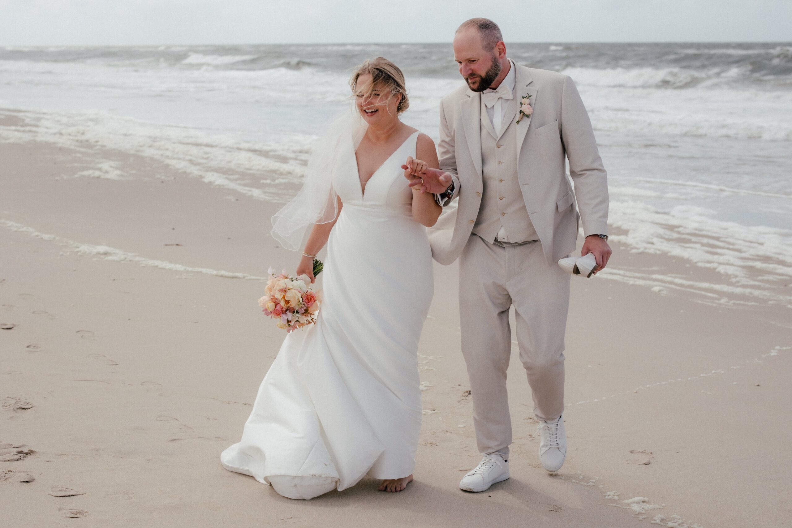 Hand in Hand über den Strand von Hamburg (Sylt) als Brautpaar. Angie Hochzeitsfotografin in Hamburg.