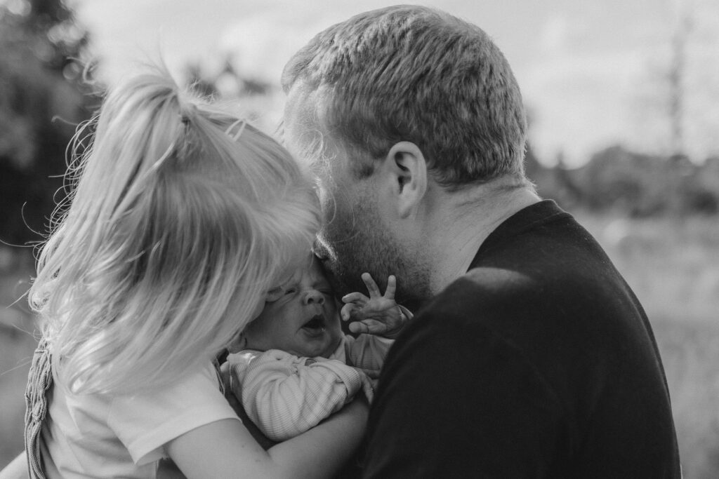 Nahaufnahme vom Vater mit seinem Neugeborenen und seiner Tochter. Familienfotografie Hamburg.