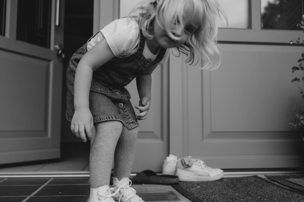 Familienfotografie Hamburg. Schwarz-Weiß-Bild eines blonden Mädchens am Eingang ihres Zuhause.